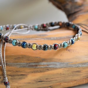 May include: A gray braided bracelet with colorful beads. The beads are blue, green, yellow, and red.