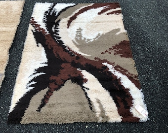 May include: A brown, white and black shag rug with a swirling abstract pattern. The rug has a fringe border.