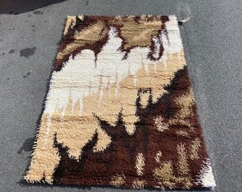 May include: A brown, beige and white shag rug with an abstract design. The rug has a long, shaggy pile and is made of a soft, plush material.