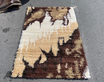 May include: A brown, beige and white shag rug with an abstract design. The rug has a long, rectangular shape and is made of a soft, fluffy material.