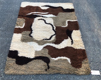 May include: A brown, beige and white shag rug with a geometric pattern. The rug has a modern, abstract design.