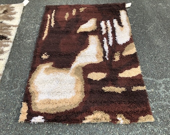 May include: A brown, beige and white shag rug with an abstract design. The rug has a thick pile and a modern, geometric pattern.