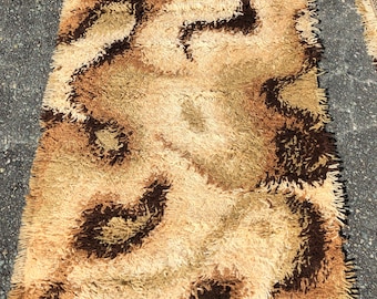 May include: Rectangular shag rug with a swirling pattern in shades of brown, tan, and cream. The rug has a textured, plush surface and a fringed edge. The tag reads "HP#252 28x45" (approximately 71 x 114 cm).