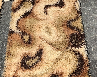 May include: A brown, beige and cream shag rug with a swirling pattern. The rug has a fringe border.
