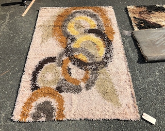 May include: A vintage shag rug with a pink background and a pattern of brown, beige, and yellow circles. The rug has a fringed edge.