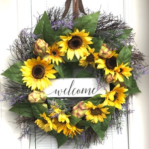 Pu&ograve; includere: Una ghirlanda di girasoli con un cartello di benvenuto. La ghirlanda &egrave; fatta di girasoli artificiali, verde e fiori viola. Il cartello &egrave; bianco con lettere nere.