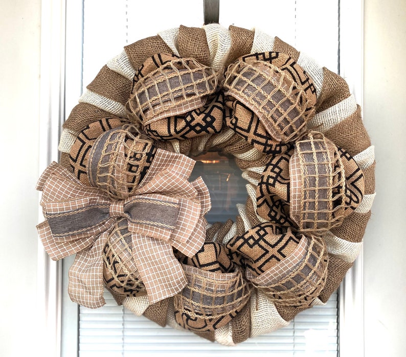 May include: A burlap wreath with a brown and white checkered bow and brown and black geometric patterned fabric accents.