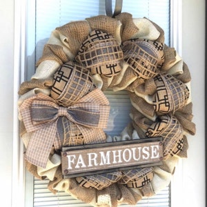 May include: A burlap and beige wreath with a brown and white checkered bow and a wooden sign that says "FARMHOUSE".