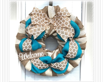 May include: A burlap and turquoise wreath with a large bow and a sign that says "Welcome".