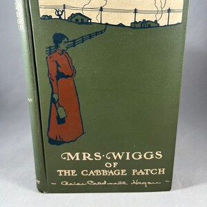 May include: A green book cover with a black and white illustration of a woman walking down a path. The title of the book is "Mrs. Wiggs of the Cabbage Patch" by "Alice Caldwell Hegan".