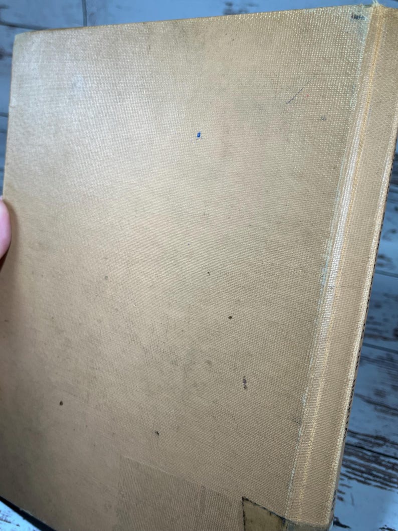 May include: A tan-colored book with a textured cover and a white spine. The book is slightly worn and has a few small dark spots on the cover.