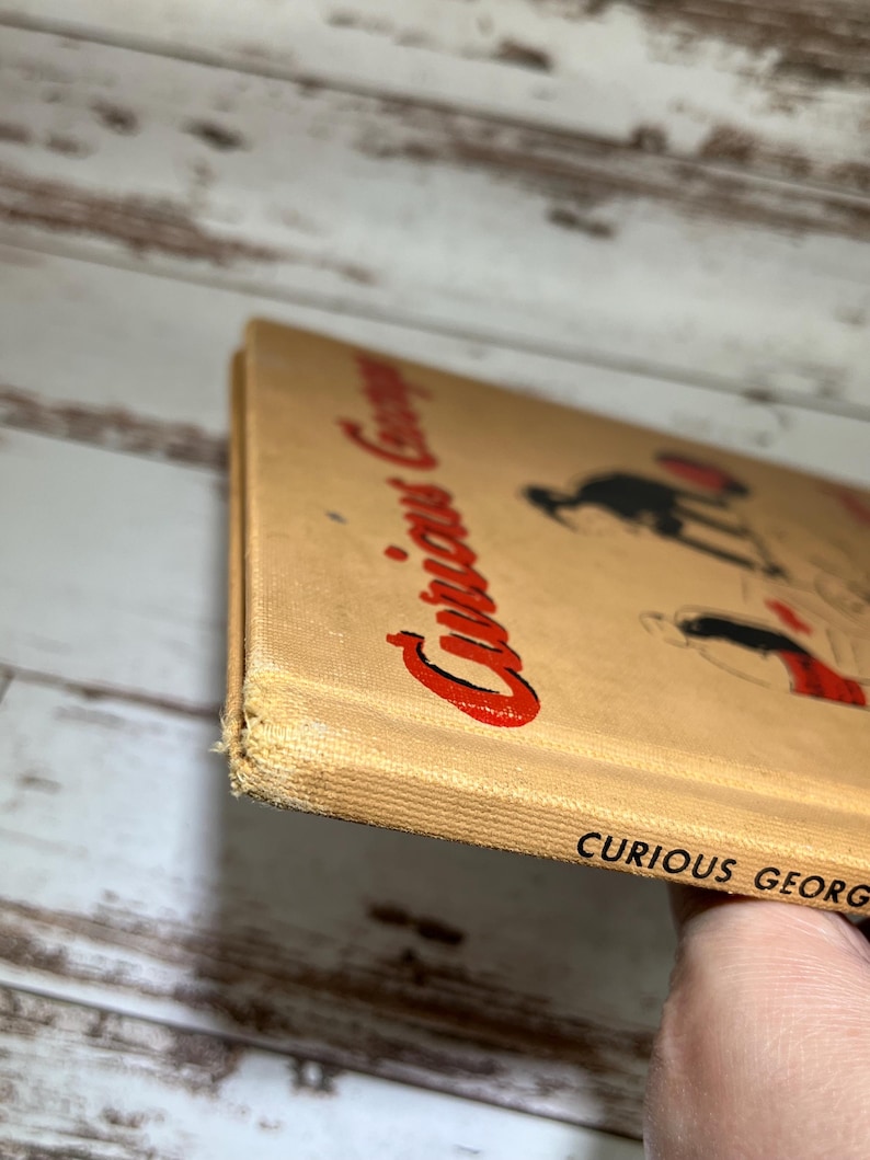 May include: A vintage hardcover book titled "Curious George" with a red and white illustration of Curious George on the cover. The book is in good condition with some wear and tear on the edges.