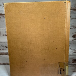 May include: A tan-colored hardcover book with a worn, textured cover. The book has a small, white label on the bottom right corner with the number "116" printed on it.