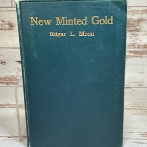 May include: A teal-colored book titled "New Minted Gold" by Edgar L. Moon. The title and author's name are in gold lettering. The book has a slightly worn appearance.