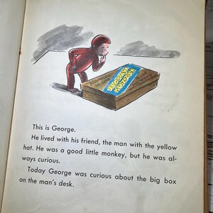 May include: A red monkey wearing a red shirt is looking at a large box with the words "Jigsaw Puzzle" on it. The box is made of wood and has a blue and white label.