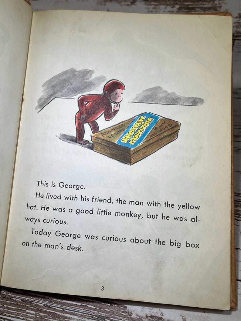May include: A red monkey wearing a red shirt is looking at a large box with the words "Jigsaw Puzzle" on it. The box is made of wood and has a blue and white label.