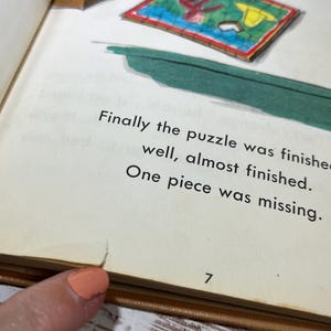 May include: A close-up of a page from a children's book. The page features an illustration of a puzzle with a missing piece. The text on the page reads: "Finally the puzzle was finished well, almost finished. One piece was missing." The page number is 7.