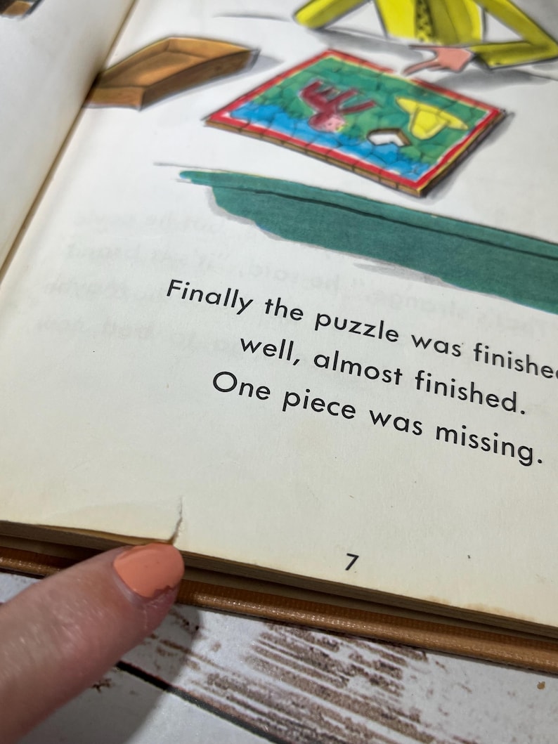 May include: A close-up of a page from a children's book. The page features an illustration of a puzzle with a missing piece. The text on the page reads: "Finally the puzzle was finished well, almost finished. One piece was missing." The page number is 7.
