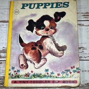 May include: Vintage children's book titled "PUPPIES" with a cartoon puppy illustration on the cover. The cover features a brown, white, and black puppy jumping in a field of flowers. The book is a "TINY-TODDLER ELF BOOK" and is priced at 25 cents.