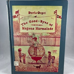 May include: A blue book with a yellow cover featuring an illustration of children waving goodbye from a boat. The title of the book is "The Good-Byes of Magnus Marmalade" by Doris Orgel.
