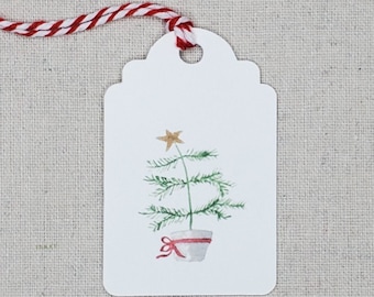 May include: White gift tag with a watercolor illustration of a small potted Christmas tree with a gold star on top. The tree is green and the pot is white with a red ribbon.