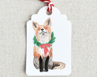 May include: A white gift tag with a watercolor illustration of a fox wearing a green wreath and a red bow. The fox is sitting and looking up.