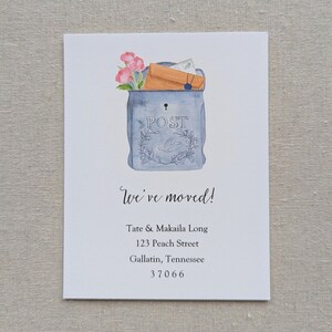 May include: A watercolor illustration of a blue mailbox with a white "POST" sign. The mailbox is overflowing with envelopes and flowers. The text "We've moved!" is written in cursive below the mailbox, followed by the new address: Tate & Makaila Long, 123 Peach Street, Gallatin, Tennessee 37066.