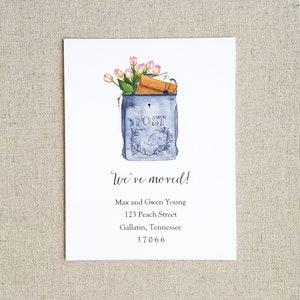 May include: A blue and white mailbox with a floral arrangement of pink tulips and a brown envelope sticking out of the top. The mailbox has the word "POST" written on it. The text "We've moved!" is written in cursive below the mailbox. The text "Max and Gwen Young, 123 Peach Street, Gallatin, Tennessee 37066" is written below the cursive text.
