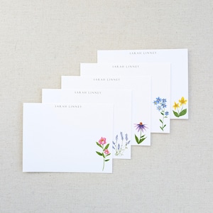 May include: White notepads with floral illustrations and the name "SARAH LINNEY" printed at the top. The floral designs include pink, purple, blue, and yellow flowers. The notepads are arranged in a layered pattern.