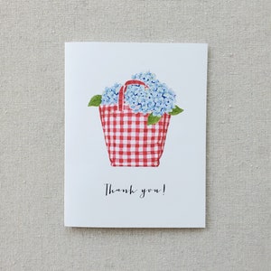 May include: A red and white gingham tote bag filled with blue hydrangeas. The bag has a red handle and the text "Thank you!" is written below the bag.