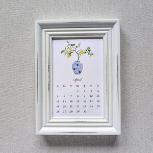 May include: A white framed calendar for April. The calendar features a watercolor illustration of a lemon tree in a blue and white vase. The word "April" is written in cursive above the calendar dates.