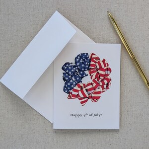 May include: A greeting card with a wreath made of red, white, and blue ribbon bows. The ribbon is patterned with stars and stripes. The text on the card reads "Happy 4th of July!"