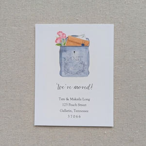 May include: A watercolor illustration of a blue mailbox with a brown envelope and pink flowers sticking out of the top. The mailbox has the word "POST" written on it. The text "We've moved!" is written below the mailbox, followed by the address "Tate & Makaila Long, 123 Peach Street, Gallatin, Tennessee 37066".