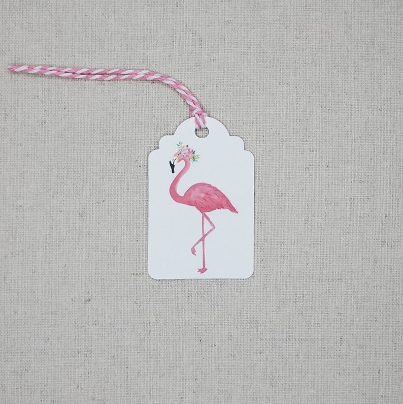 K&ouml;nnte beinhalten: Geschenk-Etikett mit einem rosa Flamingo, der eine Blumenkrone tr&auml;gt. Das Etikett ist wei&szlig; mit einem gewellten Rand und einem rosa-wei&szlig;en Band.
