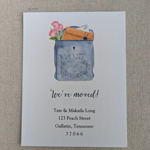 May include: A watercolor illustration of a blue mailbox with a brown envelope and pink flowers inside. The text "We've moved!" is below the mailbox, followed by the address "Tate & Makaila Long, 123 Peach Street, Gallatin, Tennessee 37066".