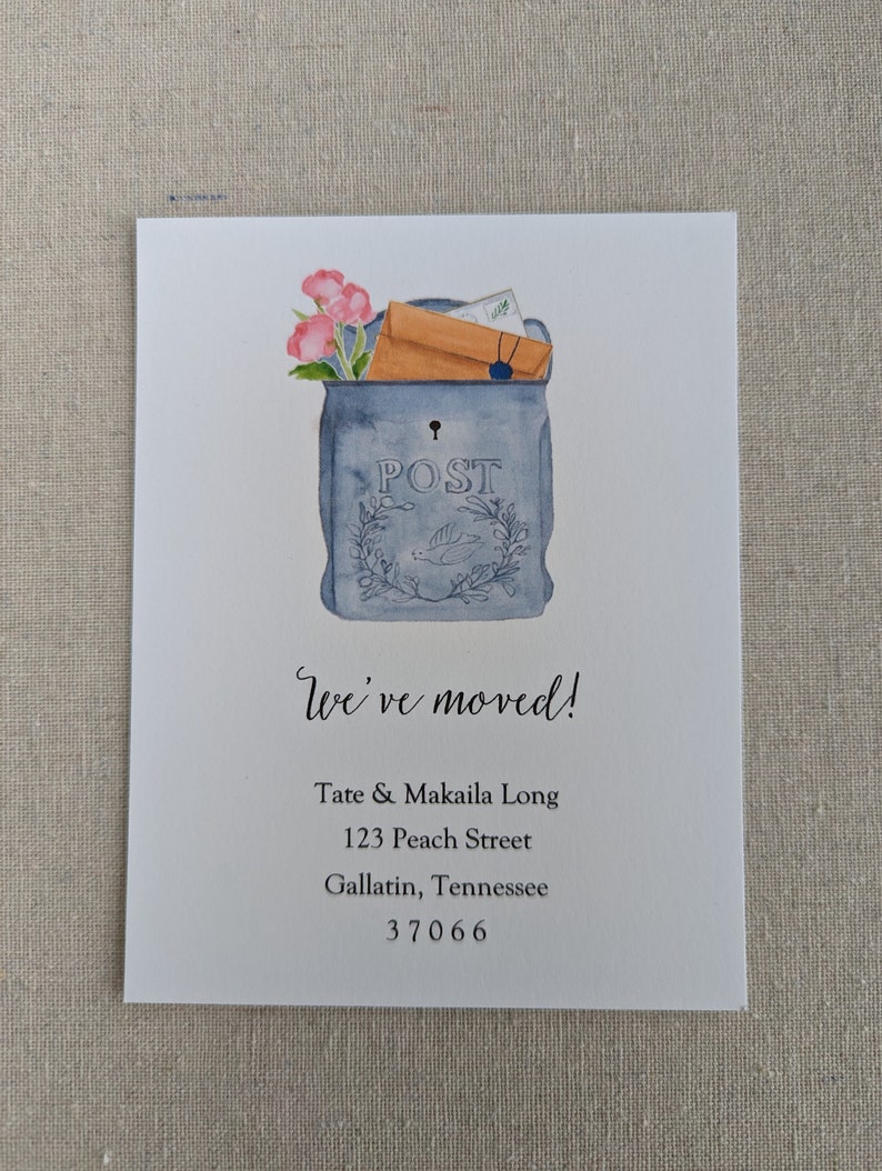May include: A watercolor illustration of a blue mailbox with a brown envelope and pink flowers inside. The text "We've moved!" is below the mailbox, followed by the address "Tate & Makaila Long, 123 Peach Street, Gallatin, Tennessee 37066".