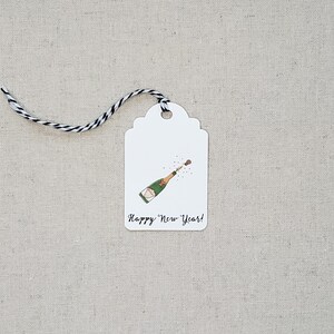 May include: White gift tag with a black and white string. The tag has a drawing of a champagne bottle popping with the text "Happy New Year!"