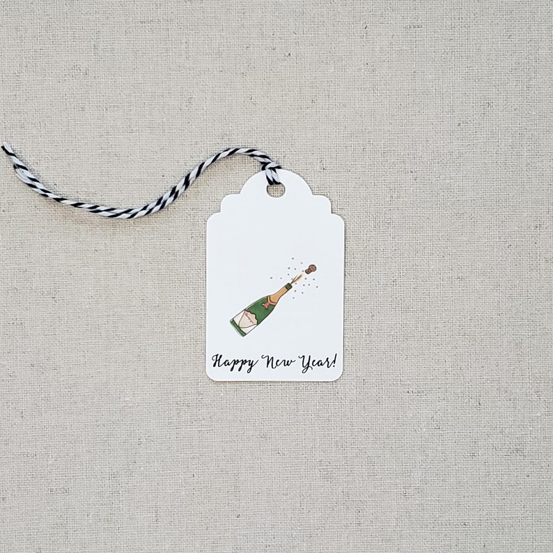 May include: White gift tag with a black and white string. The tag has a drawing of a champagne bottle popping with the text "Happy New Year!"