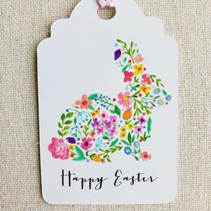 Puede incluir: Etiqueta de regalo blanca con un dise&ntilde;o de conejo floral y el texto "Feliz Pascua".