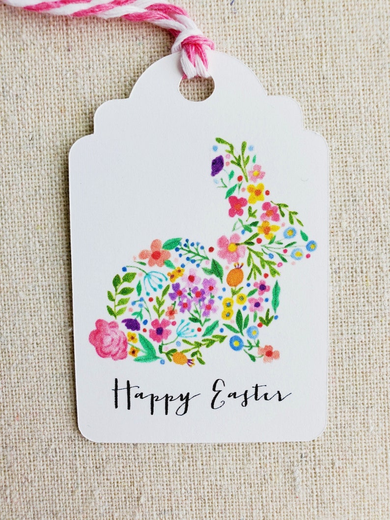 Puede incluir: Etiqueta de regalo blanca con un dise&ntilde;o de conejo floral y el texto "Feliz Pascua".