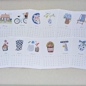 May include: A watercolor calendar featuring monthly illustrations. January shows a house, February a bicycle, March seashells, April a vase with lemons, May a basket of flowers, and June a beach chair. July shows ice cream, August a checkered pattern, September a nautical theme, October a flower basket, November an apron, and December an ornament.