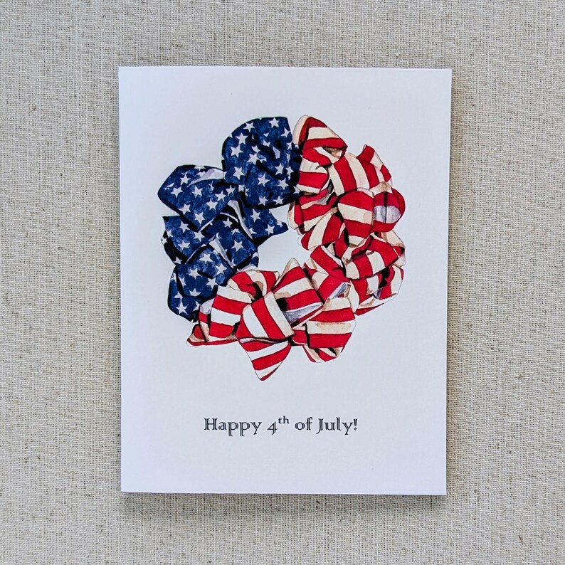 May include: A white card with a red, white, and blue fabric wreath in the center. The wreath is made of fabric strips with stars and stripes. The text "Happy 4th of July!" is printed below the wreath.
