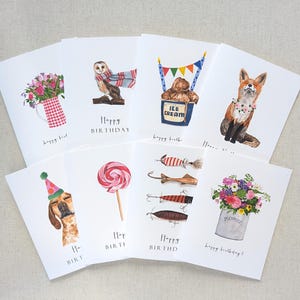May include: Set of ten illustrated birthday cards featuring various designs, including a barn owl, a fox, a dog wearing a party hat, a lollipop, fishing lures, a bucket of flowers, and a bear in an ice cream container. The cards have the text "Happy Birthday" or variations of it.