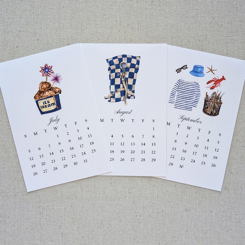 May include: Three seasonal calendar pages with watercolor illustrations. July features ice cream, August shows a checkered pattern with scissors, and September displays nautical elements. Each page includes a month name and calendar dates.
