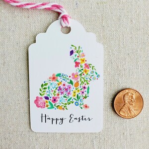 Puede incluir: Etiqueta de regalo blanca con un dise&ntilde;o de conejo floral y el texto "Feliz Pascua".