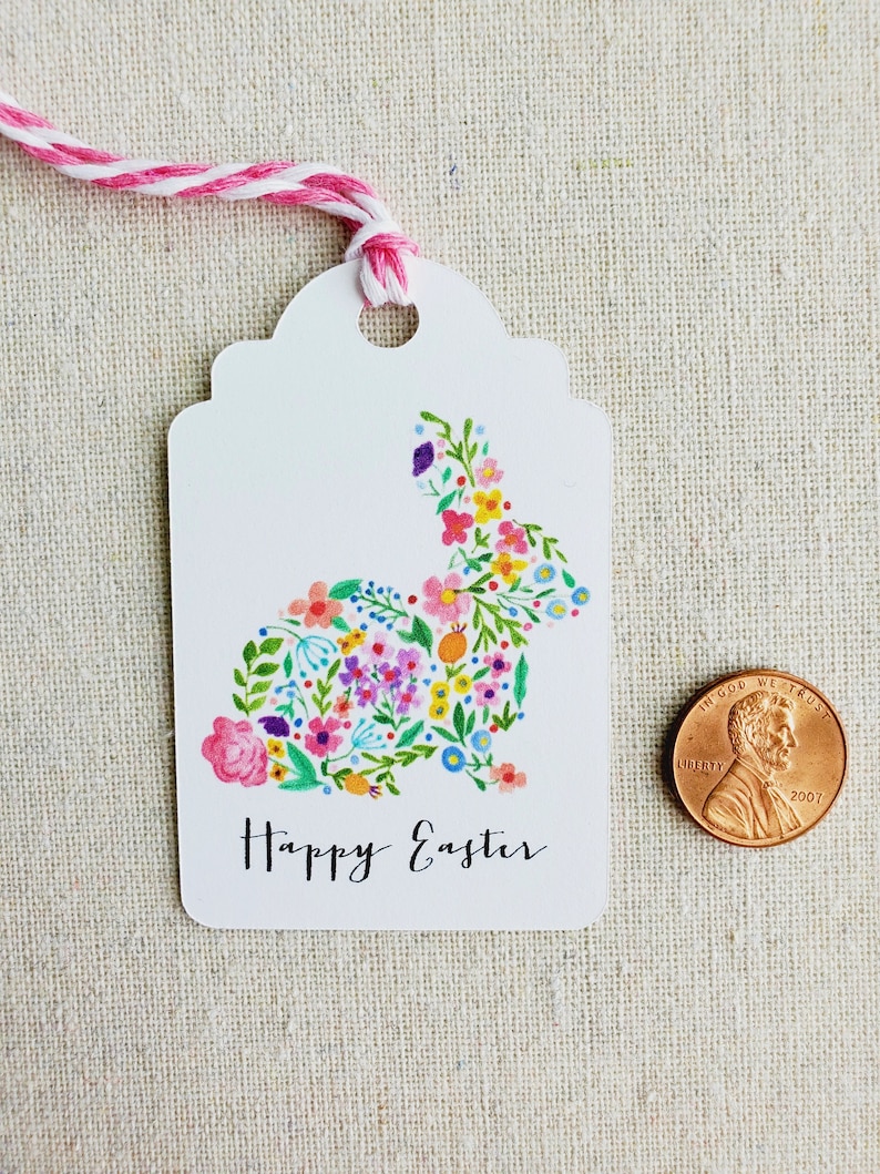 Puede incluir: Etiqueta de regalo blanca con un dise&ntilde;o de conejo floral y el texto "Feliz Pascua".