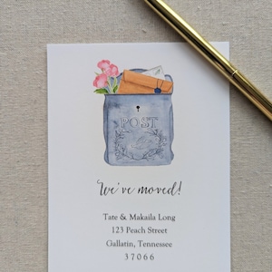 May include: A watercolor illustration of a blue mailbox with a white bird and flowers. The mailbox has the word "POST" on it. The text "We've moved!" is written below the mailbox, followed by the address "Tate & Makaila Long, 123 Peach Street, Gallatin, Tennessee 37066".