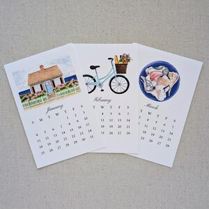 May include: Three watercolor art prints of monthly calendars. January shows a house, February a bicycle with a basket, and March seashells. Each calendar has a white background with the month's name and dates.