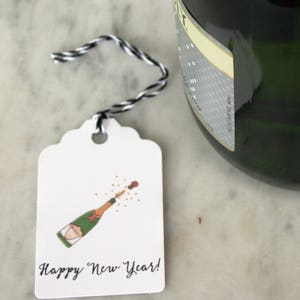 May include: A white gift tag with a hand-drawn illustration of a champagne bottle popping with a cork and a message that reads "Happy New Year!"