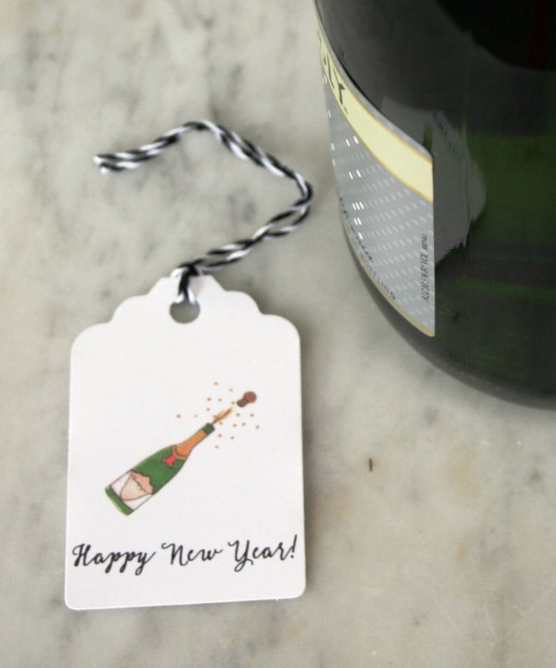 May include: A white gift tag with a hand-drawn illustration of a champagne bottle popping with a cork and a message that reads "Happy New Year!"